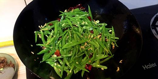 放入姜、蒜、干辣椒煸香，随后放煮熟的豆角混合均匀。