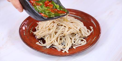 4.焯好的金针菇摆入盘中，倒入调好的料汁，再倒入备用的辣椒和小葱碎，搅拌均匀就可以开吃啦！